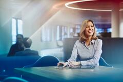 Business woman at a desk with her phone and tablet, smiling. Primary color: blue.